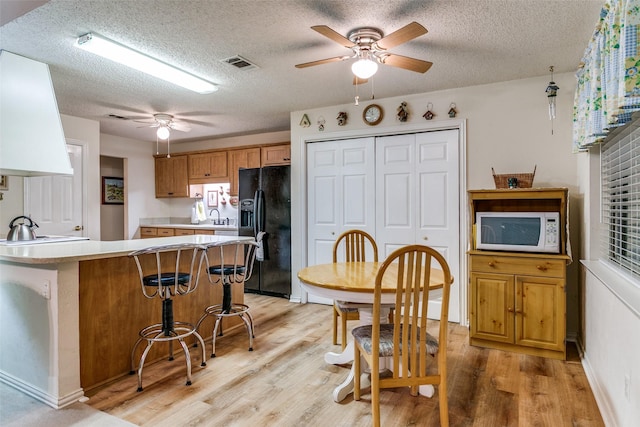 5312 Vermillion Trl, Arlington, TX 76017 - kitchen with white microwave, black refrigerator with ice dispenser, a ceiling fan, light wood-style flooring, and light countertops