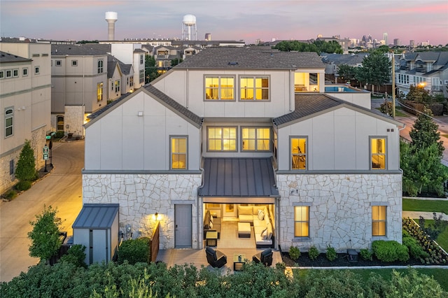 5495 Ashby Grove St, Dallas, TX 75209 - back of house at dusk with stone siding, a standing seam roof, a metal roof, and roof with shingles