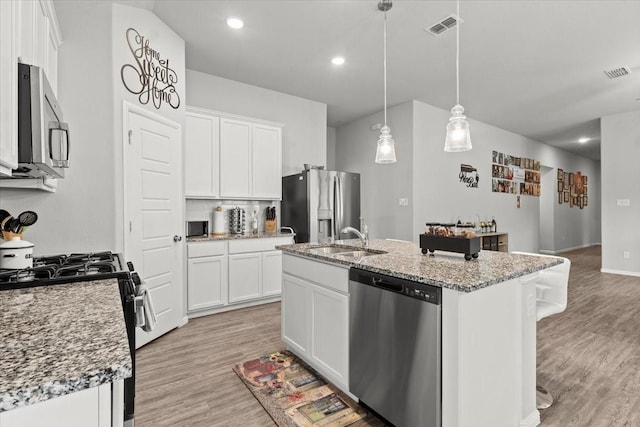 7118 Pampas Pl, Grand Prairie, TX 76804 - kitchen with appliances with stainless steel finishes, light wood-style flooring, a center island with sink, white cabinets, and recessed lighting