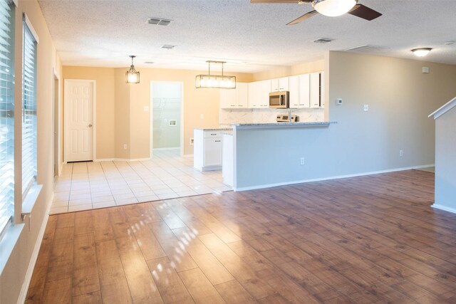 1565 Laurel Hall Ln, Little Elm, TX 75068 - kitchen featuring stainless steel microwave, light wood-style floors, a ceiling fan, white cabinetry, and a textured ceiling