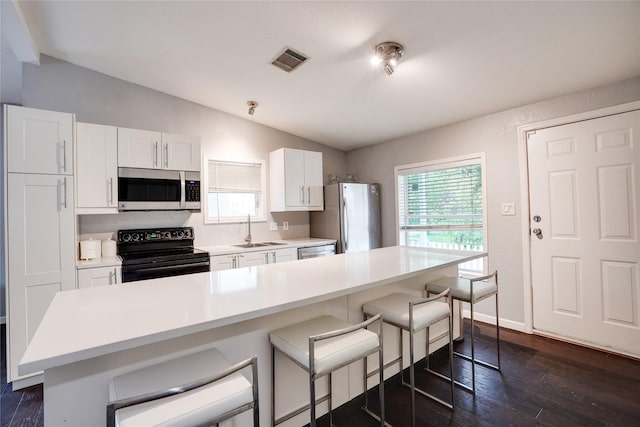 5712 Hudson St, Dallas, TX 75206 - kitchen featuring appliances with stainless steel finishes, vaulted ceiling, a kitchen bar, white cabinetry, and light countertops
