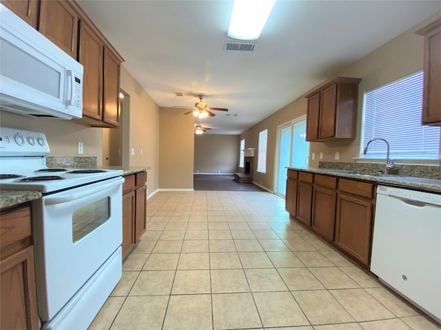 1125 Greenbend Dr, Denton, TX 76210 - kitchen with white appliances, a ceiling fan, light tile patterned flooring, brown cabinetry, and dark stone countertops