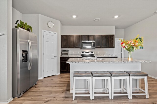 7209 Guadalupe Rd, China Spring, TX 76633 - kitchen featuring stainless steel appliances, light wood finished floors, dark brown cabinets, and a kitchen breakfast bar