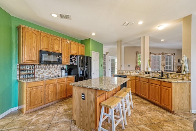 9513 Tiger Dr, Plano, TX 75025 - kitchen with black appliances, decorative backsplash, a kitchen island, a breakfast bar, and light stone countertops