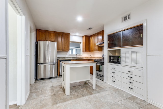 632 Sherwood Dr, Richardson, TX 75080 - kitchen featuring appliances with stainless steel finishes, brown cabinets, a kitchen island, and under cabinet range hood