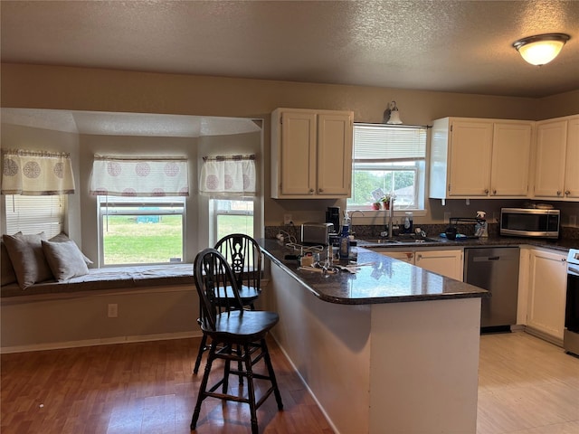 4052 Country Meadows Cir, Granbury, TX 76049 - kitchen featuring appliances with stainless steel finishes, a peninsula, white cabinetry, a kitchen breakfast bar, and a textured ceiling