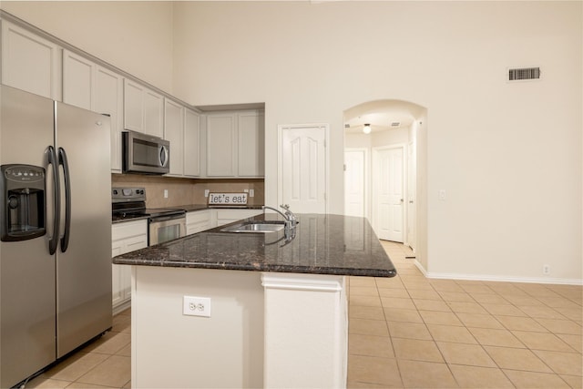 2401 Fawn Meadow Dr, Little Elm, TX 75068 - kitchen featuring appliances with stainless steel finishes, a towering ceiling, light tile patterned flooring, dark stone countertops, and backsplash