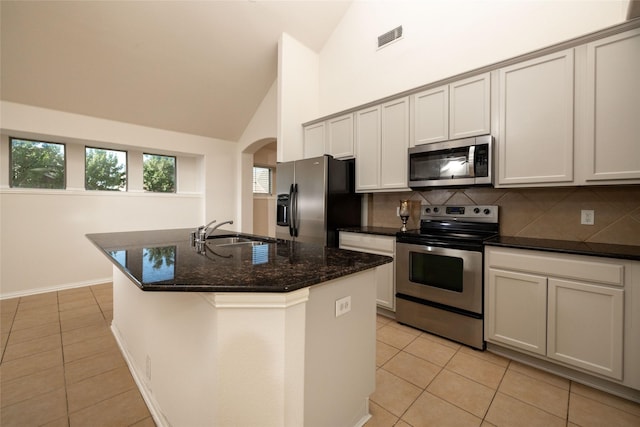 2401 Fawn Meadow Dr, Little Elm, TX 75068 - kitchen with appliances with stainless steel finishes, light tile patterned floors, backsplash, high vaulted ceiling, and arched walkways