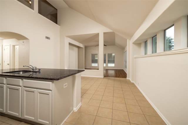 2401 Fawn Meadow Dr, Little Elm, TX 75068 - kitchen with lofted ceiling, light tile patterned floors, dark stone counters, arched walkways, and a kitchen island with sink