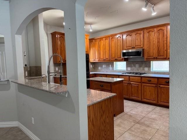 3840 W Pioneer Dr, Irving, TX 75061 - kitchen with stainless steel microwave, backsplash, gas stovetop, and brown cabinetry