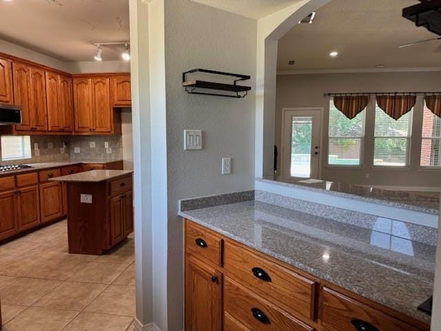 3840 W Pioneer Dr, Irving, TX 75061 - kitchen featuring brown cabinets, light tile patterned flooring, arched walkways, decorative backsplash, and stovetop