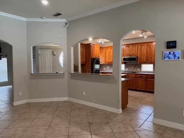 3840 W Pioneer Dr, Irving, TX 75061 - kitchen featuring stainless steel appliances, brown cabinetry, crown molding, light tile patterned floors, and backsplash