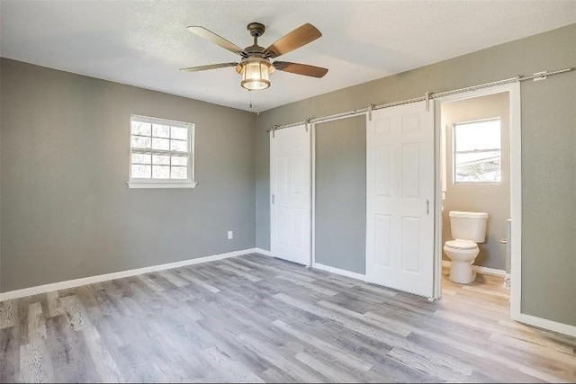3501 NE 10th St, Mineral Wells, TX 76067 - unfurnished bedroom featuring a barn door, wood finished floors, ensuite bath, and ceiling fan