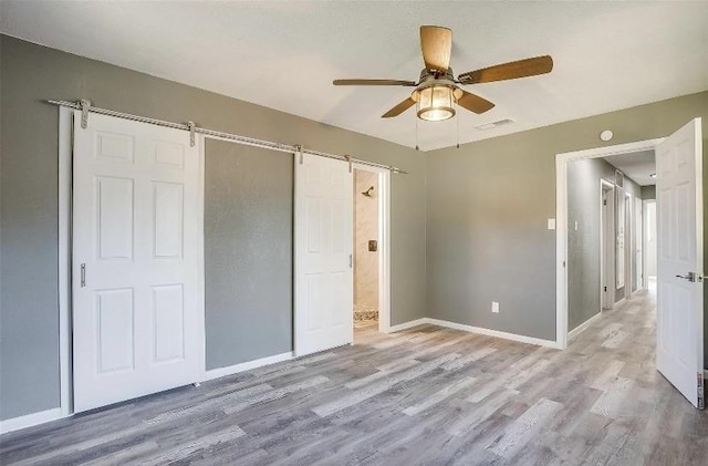 3501 NE 10th St, Mineral Wells, TX 76067 - unfurnished bedroom with a barn door, light wood-style flooring, and ceiling fan