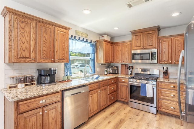 1413 White Way, Mckinney, TX 75069 - kitchen featuring stainless steel appliances, backsplash, light wood-style flooring, brown cabinets, and light stone counters