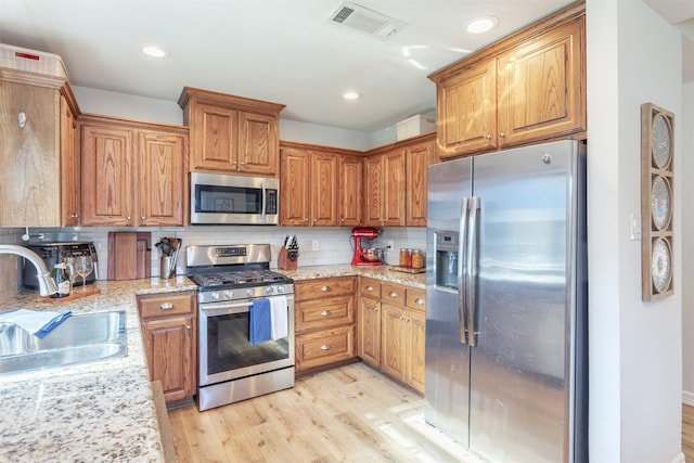 1413 White Way, Mckinney, TX 75069 - kitchen with appliances with stainless steel finishes, light wood finished floors, backsplash, brown cabinetry, and light stone counters