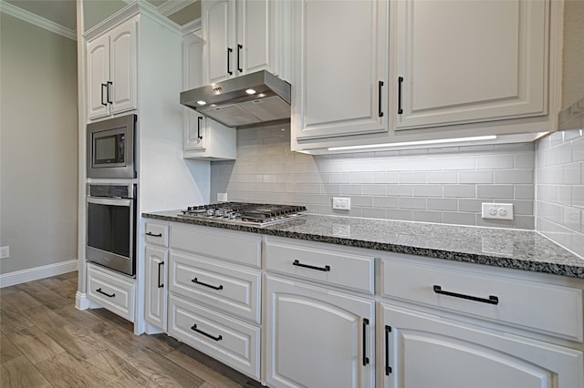 233 Cross Fox Ln, Aledo, TX 76008 - kitchen with appliances with stainless steel finishes, under cabinet range hood, white cabinetry, ornamental molding, and dark stone countertops