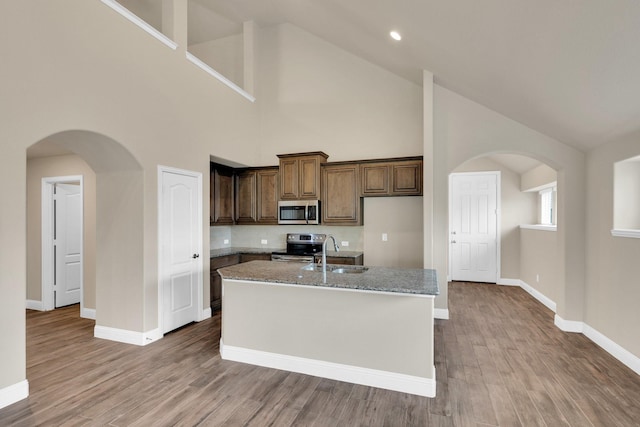 350 Windsor St, Waxahachie, TX 75165 - kitchen featuring appliances with stainless steel finishes, high vaulted ceiling, wood finished floors, an island with sink, and light stone countertops