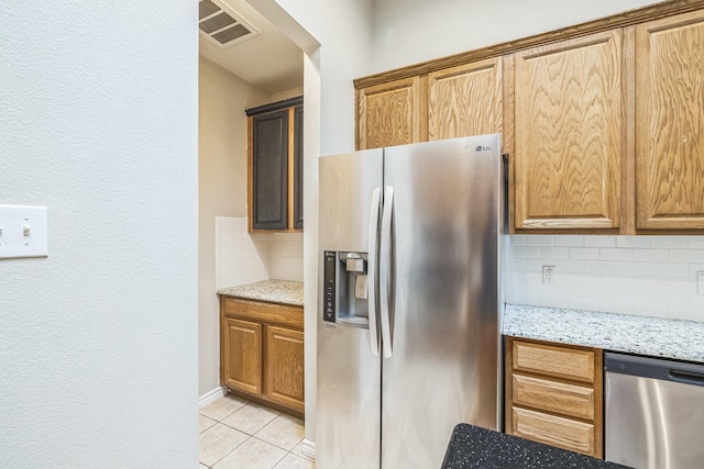 4471 Chandler Dr, Frisco, TX 75034 - kitchen with stainless steel appliances, backsplash, light tile patterned flooring, light stone counters, and brown cabinetry