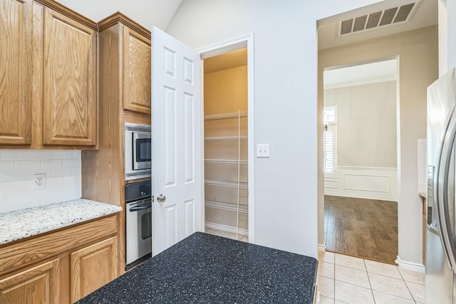 4471 Chandler Dr, Frisco, TX 75034 - kitchen with stainless steel appliances, light stone countertops, decorative backsplash, light tile patterned flooring, and brown cabinets