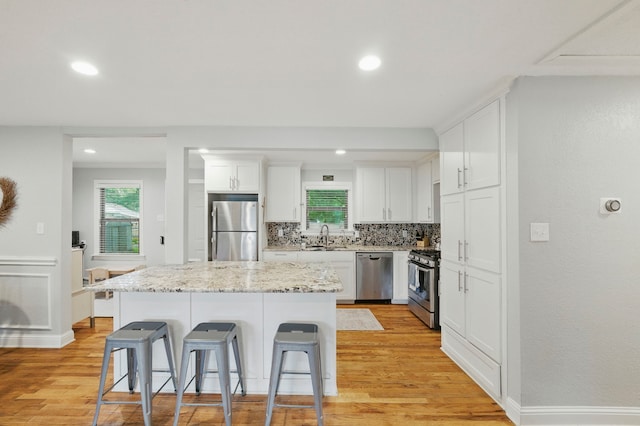 3000 Binyon St, Fort Worth, TX 76133 - kitchen with stainless steel appliances, a breakfast bar area, light wood-style floors, backsplash, and white cabinetry