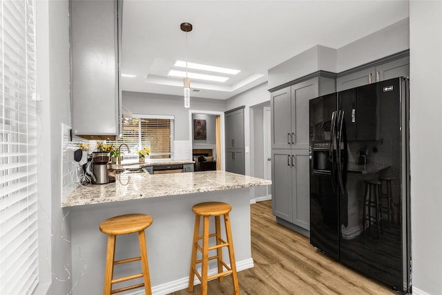 14902 Le Grande Dr, Addison, TX 75001 - kitchen with black refrigerator with ice dispenser, gray cabinetry, light wood-type flooring, a peninsula, and light stone countertops