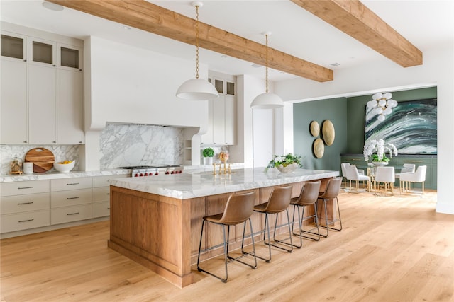 7226 Colgate Ave, Dallas, TX 75225 - kitchen with tasteful backsplash, a large island, light wood-type flooring, a kitchen bar, and decorative light fixtures