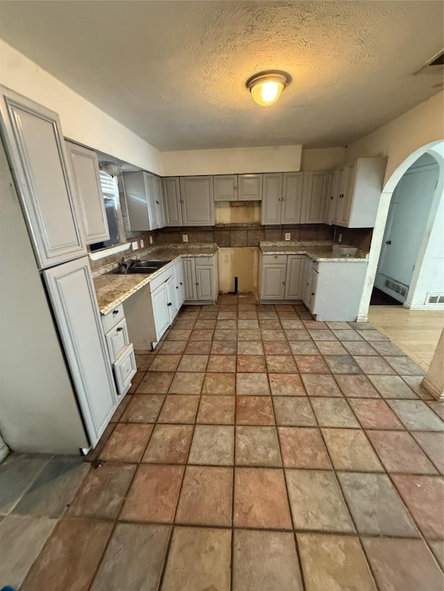 1421 Richard St, Mesquite, TX 75149 - kitchen with arched walkways, gray cabinetry, a textured ceiling, decorative backsplash, and light stone finish floors