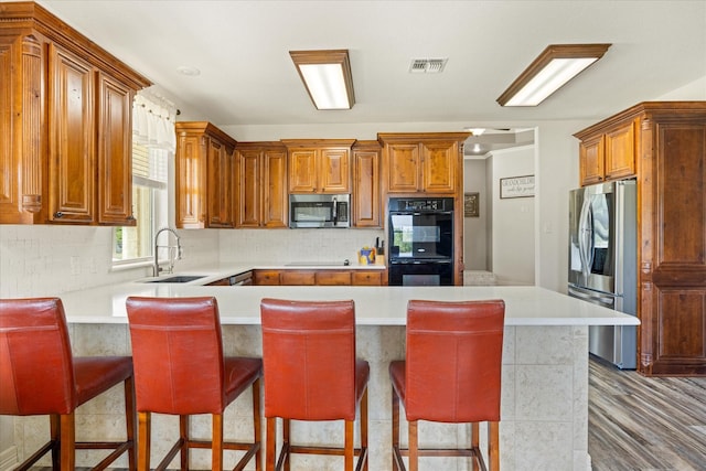 2030 Hills Ct, Stephenville, TX 76401 - kitchen featuring black appliances, a peninsula, light countertops, decorative backsplash, and brown cabinetry