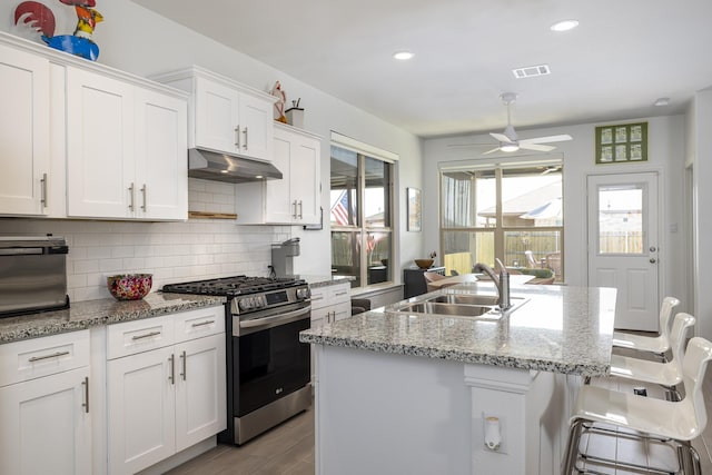 9657 Alderleaf Trl, Fort Worth, TX 76036 - kitchen featuring stainless steel gas range oven, under cabinet range hood, a ceiling fan, backsplash, and white cabinets