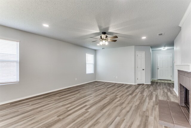 8732 Hunters Trl, Fort Worth, TX 76123 - unfurnished living room with a brick fireplace, a ceiling fan, light wood-style floors, a textured ceiling, and recessed lighting