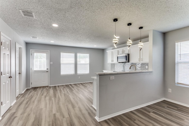 8732 Hunters Trl, Fort Worth, TX 76123 - kitchen with stainless steel microwave, light wood finished floors, white cabinetry, tasteful backsplash, and a textured ceiling