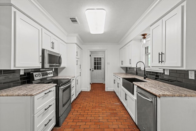 119 Locust Ct, Oak Leaf, TX 75154 - kitchen with appliances with stainless steel finishes, brick patterned flooring, ornamental molding, white cabinets, and decorative backsplash
