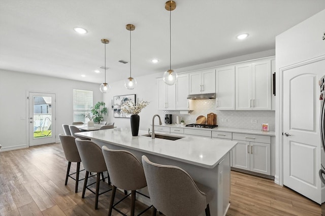 1213 Bonsmara Dr, Northlake, TX 76247 - kitchen with under cabinet range hood, a breakfast bar area, light wood finished floors, tasteful backsplash, and light countertops