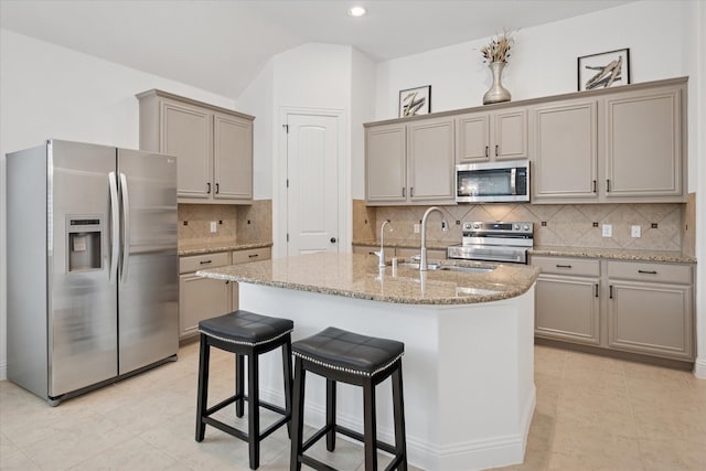 5704 Ridgeson Dr, Mckinney, TX 75071 - kitchen with stainless steel appliances, light tile patterned floors, a kitchen island with sink, light stone countertops, and vaulted ceiling