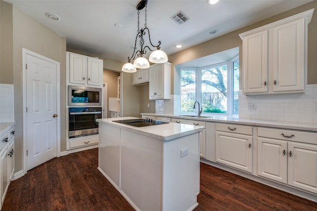 6001 Autumn Way, Mckinney, TX 75072 - kitchen featuring appliances with stainless steel finishes, dark wood finished floors, backsplash, white cabinetry, and a center island