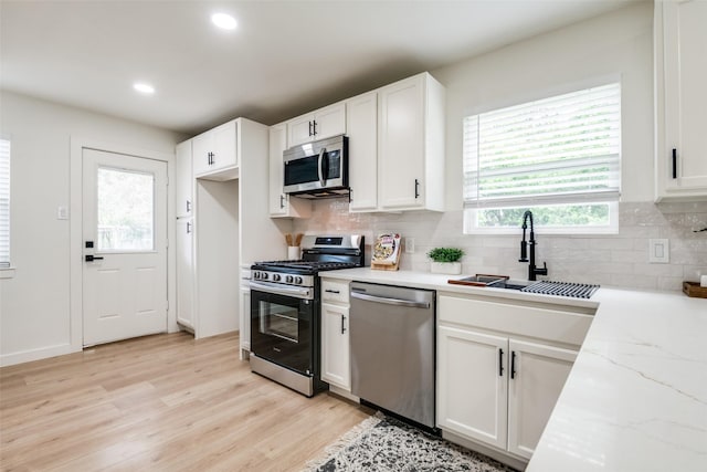 826 Nash St, Rockwall, TX 75087 - kitchen with appliances with stainless steel finishes, light wood-type flooring, white cabinetry, backsplash, and light stone countertops