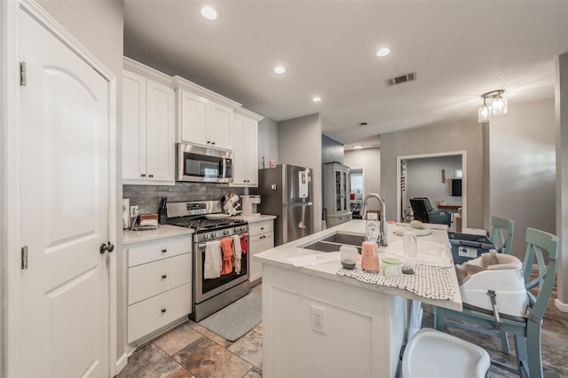 1020 Water St, Waxahachie, TX 75165 - kitchen featuring appliances with stainless steel finishes, decorative backsplash, an island with sink, a breakfast bar area, and white cabinetry