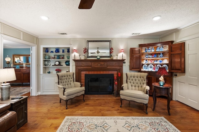 1121 W 3rd Ave, Corsicana, TX 75110 - living area featuring a ceiling fan, a textured ceiling, ornamental molding, a fireplace, and light wood-style flooring