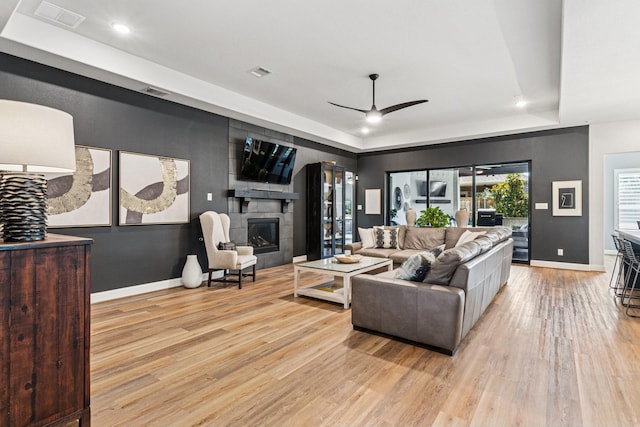 7709 Waterside, The Colony, TX 75056 - living room featuring a tray ceiling, light wood-style flooring, a ceiling fan, a glass covered fireplace, and recessed lighting