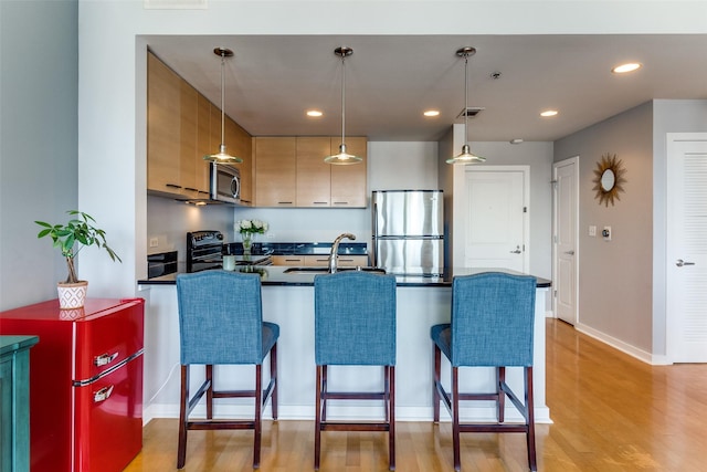 1200 Main St Unit 1402, Dallas, TX 75202 - kitchen featuring appliances with stainless steel finishes, a peninsula, dark countertops, decorative light fixtures, and light wood-type flooring