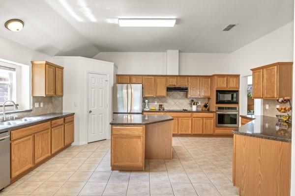 521 Willowview Dr, Saginaw, TX 76179 - kitchen with appliances with stainless steel finishes, vaulted ceiling, tasteful backsplash, under cabinet range hood, and a kitchen island