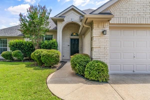 521 Willowview Dr, Saginaw, TX 76179 - view of exterior entry with an attached garage, brick siding, a yard, and concrete driveway