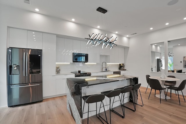 2001 N Prairie Ave Unit 106, Dallas, TX 75204 - kitchen featuring appliances with stainless steel finishes, modern cabinets, white cabinetry, light wood-style floors, and a breakfast bar