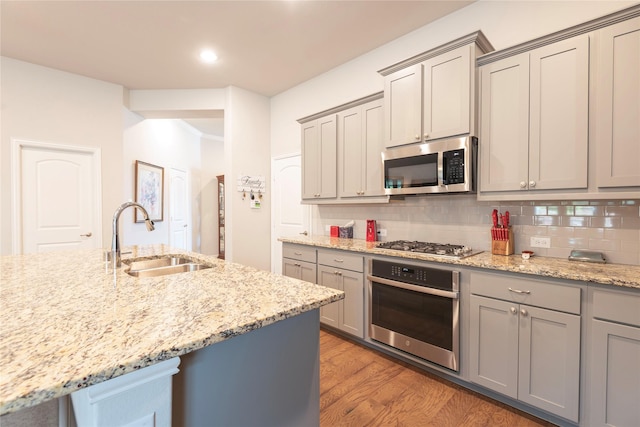 873 Mildren Ln, Fate, TX 75087 - kitchen featuring appliances with stainless steel finishes, gray cabinetry, light wood-style flooring, backsplash, and light stone countertops