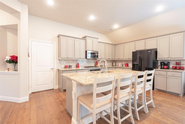 873 Mildren Ln, Fate, TX 75087 - kitchen featuring stainless steel microwave, lofted ceiling, backsplash, light wood-type flooring, and black fridge with ice dispenser