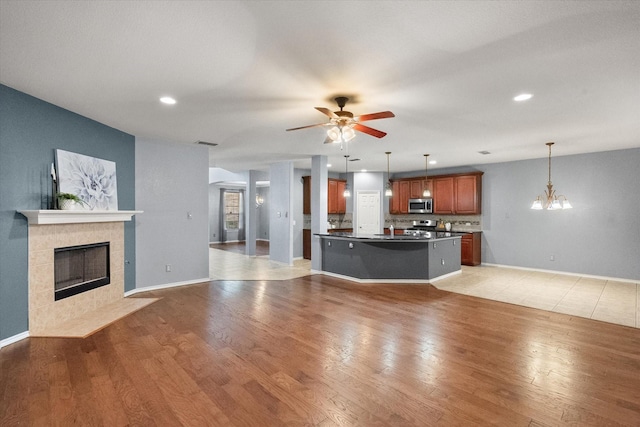 9324 Shadowfax Dr, Arlington, TX 76002 - unfurnished living room featuring a tiled fireplace, ceiling fan, recessed lighting, light wood finished floors, and a chandelier