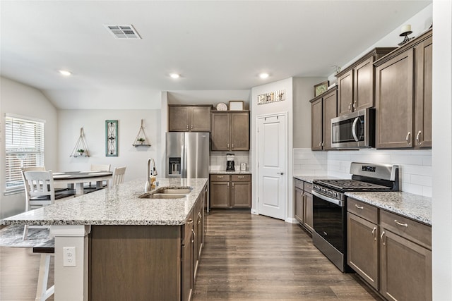 702 Stampede Ln, Princeton, TX 75407 - kitchen with appliances with stainless steel finishes, dark wood finished floors, tasteful backsplash, dark brown cabinets, and an island with sink