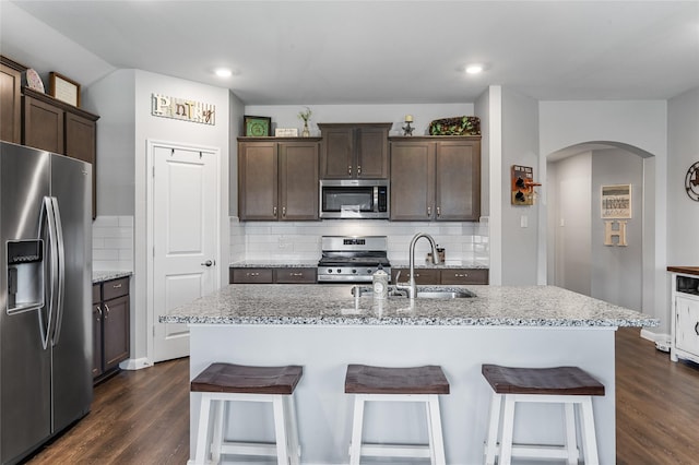 702 Stampede Ln, Princeton, TX 75407 - kitchen with stainless steel appliances, arched walkways, dark wood finished floors, dark brown cabinetry, and a kitchen breakfast bar