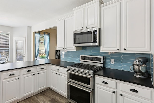 104 Northfield Cir, Hickory Creek, TX 75065 - kitchen featuring appliances with stainless steel finishes, dark countertops, tasteful backsplash, a peninsula, and dark wood-style floors